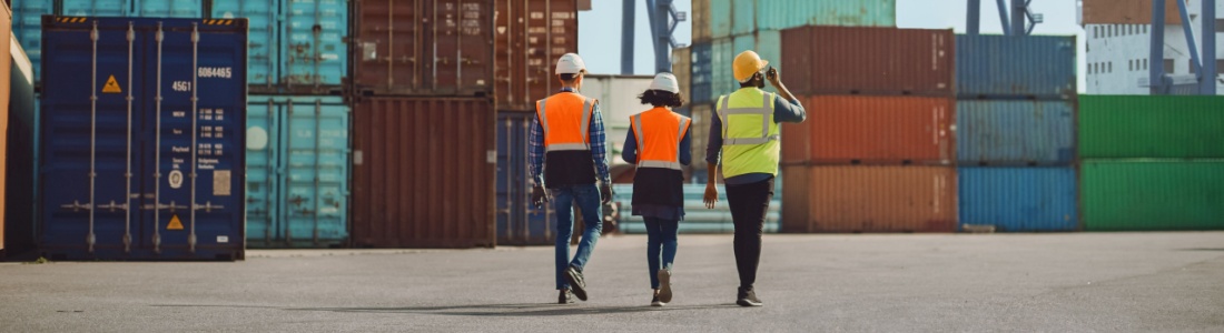 Workers walking through a shipping cargo container terminal depot.
