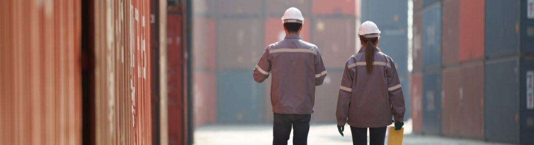 Two workers walking between shopping containers.