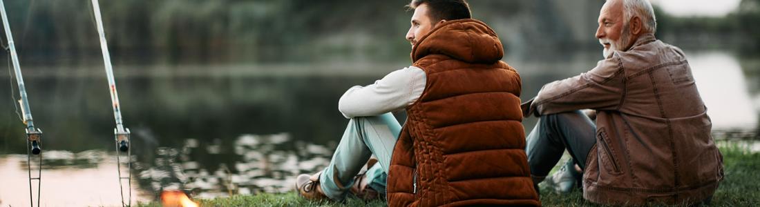 Two men sitting together and fishing by a river.