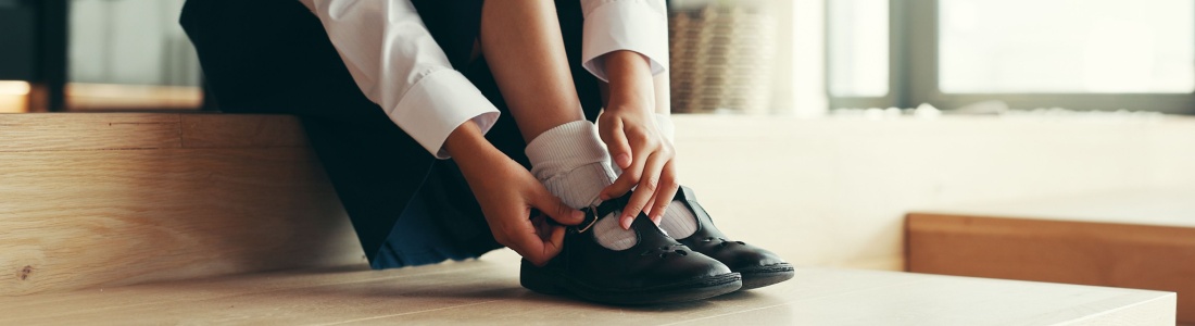 A girl putting on school shoes.
