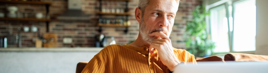 A man in his 50s thinking while using a laptop