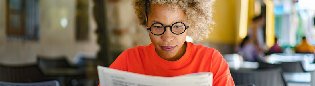 A woman reading a newspaper in a café.